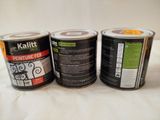 three cans of paint sitting on top of a bed next to each other