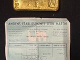 a piece of gold on a piece of paper next to a bar of gold