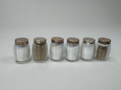 five glass salt shakers lined up in a row on a white surface