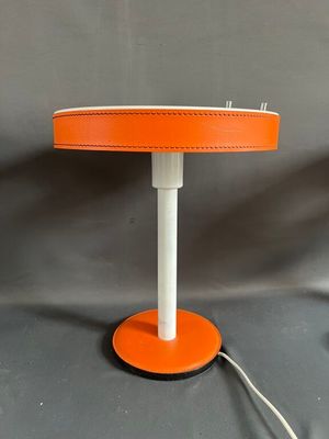 une lampe de table orange avec un pied blanc et un pied noir