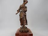 une statue antique en bronze représentant une femme tenant un oiseau, posée sur un socle en bois