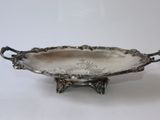 un plat ancien en argent avec des poignées, posé sur un socle, sur une surface blanche