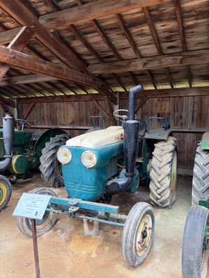 Plusieurs vieux tracteurs sont garés dans une grange où se trouve une pancarte posée par terre.