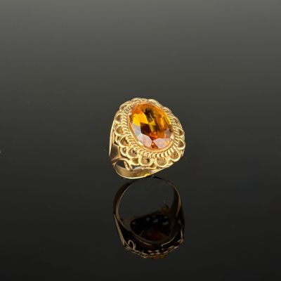a gold ring with an oval citrine stone surrounded by a filigree band