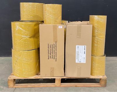 Plusieurs rouleaux de ruban adhésif jaune sont empilés sur une palette devant un mur noir.
