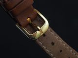 brown leather watch strap with a gold buckle on a black background