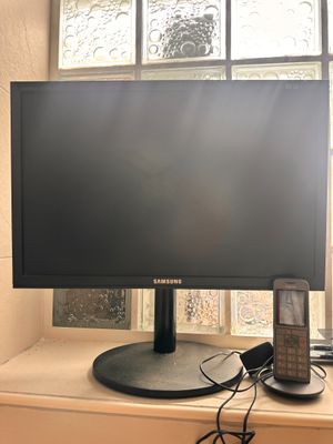 a computer monitor sitting on a window sill next to a cell phone