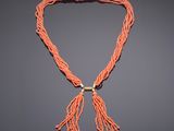 a coral colored necklace with a gold clasp and tassel