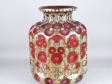 a red and gold vase sitting on a white surface