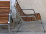 a wooden bench and a metal chair on the sidewalk