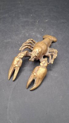 deux homards en laiton posés sur une surface noire, sur fond noir