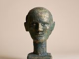 sculpture représentant une tête d'homme posée sur un socle, sur fond beige