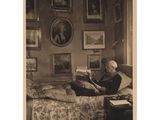 photographie en noir et blanc d'une femme assise sur un lit en train de lire un livre
