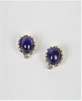 une paire de boucles d'oreilles à clous en verre violet posées sur une surface blanche