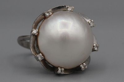 une image représentant une bague en perle blanche et diamants sur fond gris