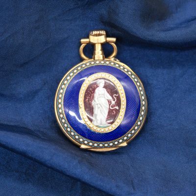 une image représentant une montre de poche bleue et dorée sur laquelle figure le portrait d'une femme