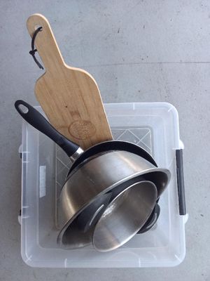 pots and pans sitting in a plastic container with a wooden spatula