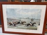 a framed picture of a horse race with jockeys and horses