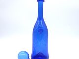 a blue glass bottle and a blue glass ball on a white surface
