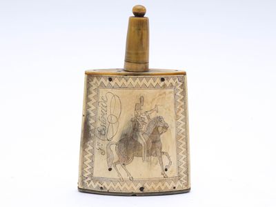 une flasque ancienne en laiton sur laquelle figure l'image d'un homme à cheval