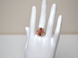 a white hand with a ring on it that has a pink and blue stone