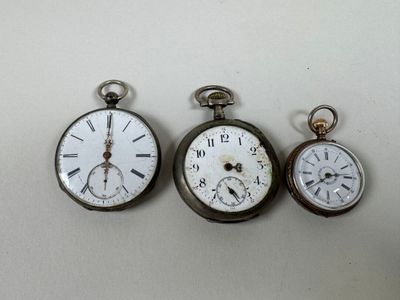 trois types différents de montres de poche posées sur une surface blanche