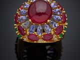 un gros plan d'une bague ornée d'une pierre rouge entourée de pierres bleues et vertes