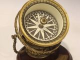 une boussole ancienne en laiton posée sur un socle en bois, sur fond blanc