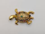 a close up of a gold turtle brooch with colorful stones