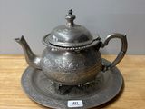 an antique silver teapot and saucer on a wooden table