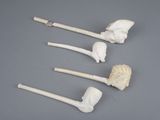 three white pipe holders with carved heads on them on a gray surface