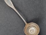 une cuillère en argent ancienne posée sur une surface noire, avec une cuillère en argent au milieu
