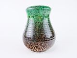 a green and black vase sitting on a white surface
