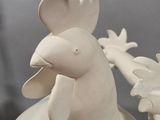 a white ceramic sculpture of a rooster holding a flower
