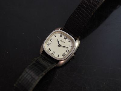 une montre en argent avec des chiffres romains, montée sur un bracelet noir