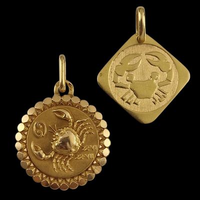a close up of two gold zodiac charms on a black background