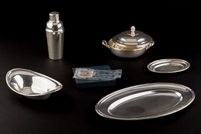 a silver plate with a spoon, a bottle, and other silverware on a table