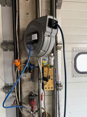 un compteur d'eau dans un garage, auquel est raccordé un tuyau d'arrosage