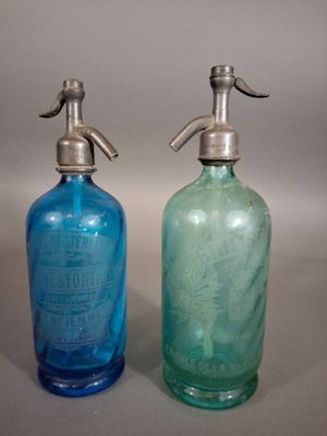 une paire de bouteilles en verre bleues et vertes, munies de poignées argentées, posées sur un support gris