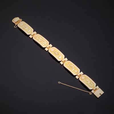 un bracelet en or orné de visages sculptés et d'une chaîne sur fond noir