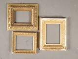 three gold picture frames on a gray wall with a mirror