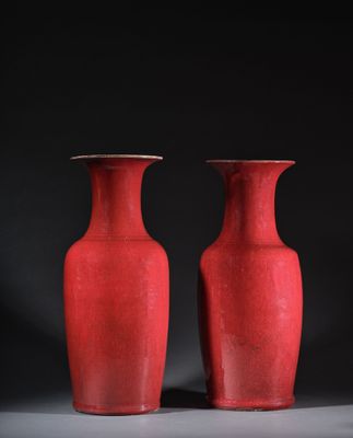 une paire de vases rouges posés sur une table, sur fond noir