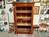 a tall wooden bookcase with glass shelves in a room