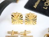 gold plated cufflinks and a black bag are on a white surface