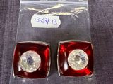 une paire de boucles d'oreilles à clous en cristal rouge et transparent, dans un emballage en plastique