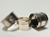three silver napkins and a silver cup on a white surface