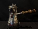 an antique silver coffee pot with a wooden handle on a black background