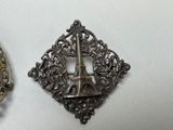 two silver brooches with a tower in the middle of them