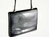 sac à main en cuir noir avec des finitions dorées et une bandoulière, sur fond blanc