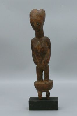 une statue en bois représentant un homme tenant un bol, posée sur un socle noir